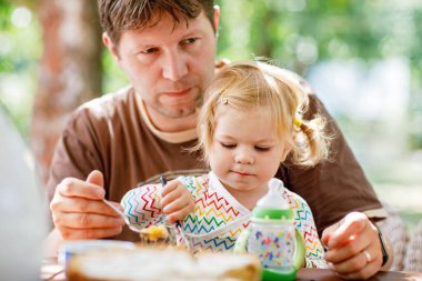 Sevimli küçük yürümeye başlayan çocuk kız restoranda besleme genç orta yaşlı baba. Arka plan üzerinde yemek çocuk evlat. Yaz saati, açık bir kafe mutlu sağlıklı aile pasta yemeye.