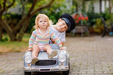 İki mutlu çocuk açık havada, yaz bahçesinde eski oyuncak arabalarıyla oynuyorlar. Çocuk, içinde küçük bir kız çocuğu olan arabayı sürüyor. Gülen ve gülümseyen çocuklar. Aile, çocukluk, yaşam tarzı konsepti.