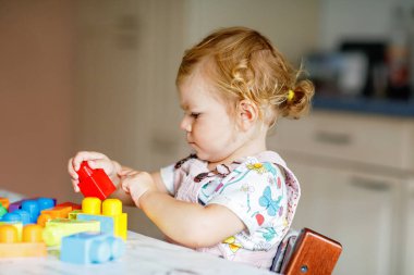 Çocuk odasında ya da evde eğitici oyuncakları olan sevimli bir kız. Mutlu sağlıklı çocuk farklı renkli plastik bloklarla eğleniyor. Sevimli bebek öğrenimi yaratma.