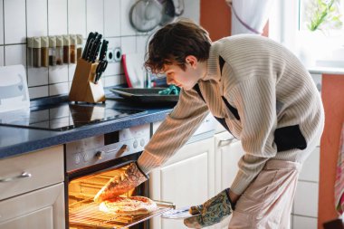 Yakışıklı genç çocuk öğle yemeği için evde pizza pişiriyor. İtalyan pizzası tutan bir genç. .