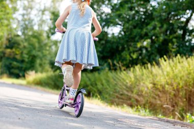 Closeup of active little preschool girl riding scooter on road in park outdoors on summer day. Seasonal child activity sport. Healthy childhood lifestyle.