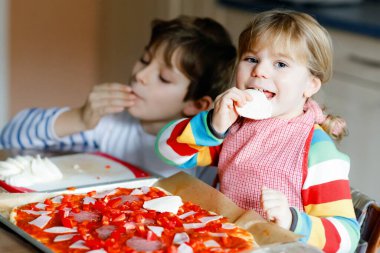 İki kardeş, evde İtalyan pizzası yapan küçük çocuklar. Şirin kız ve okul çocuğu ev mutfağında, evde eğleniyorlar. Erkek ve kız kardeş, aile yemeği hazırlıyor..