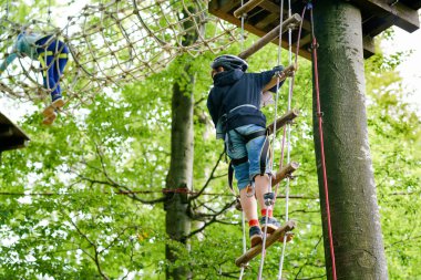 Orman macera parkında iki çocuk. Miğferli çocuklar yüksek ip üzerinde tırmanırlar. Çeviklik becerileri ve çocuklar için açık hava eğlence merkezine tırmanma. Çocuklar ve aileler için açık hava aktivitesi
