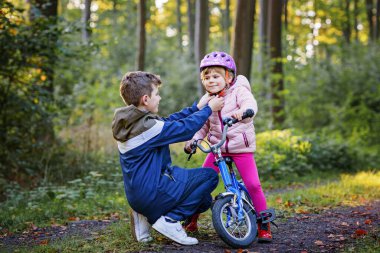 Erkek kardeş, kız kardeş, kız kardeş bisiklet kaskını kafasına taktı. Kardeş mutlu çocuk bisikleti öğretiyor ve bisikletle eğleniyor. Aktif aile fertleri açık havada. Çocuk aktivitesi.