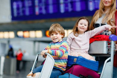 İki küçük çocuk, erkek ve kız, kardeşler ve anne havaalanında. Çocuklar, aile seyahati, uçakla tatile gitmek ve bir kadının terminalden uçmak için ittiği valizlerle tramvayda beklemek.