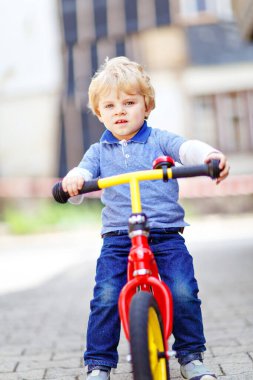 Renkli elbiseli aktif sarışın çocuk denge kuruyor ve bisikleti ya da bisikleti bahçede öğreniyor. Küçük çocuk sıcak yaz gününde rüya görüyor ve eğleniyor. Çocuklar için açık hava hareket oyunu