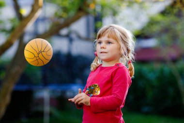 Dışarıda topla oynayan küçük sevimli bir kız. Gülümseyen çocuk yakalayıp fırlatıyor, gülüyor ve spor yapıyor. Çocuklar ve çocuklarla aktif eğlence.