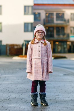 Gözlüklü, pembe paltolu ve şapkalı küçük bir kızın portresi. Mutlu çocuk soğuk güneşli bir günde