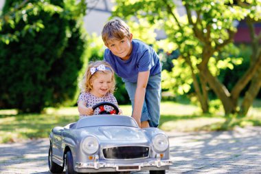 İki mutlu çocuk açık havada, yaz bahçesinde eski oyuncak arabalarıyla oynuyorlar. Küçük bir kızla araba süren bir çocuk, içinde de tatlı bir kız kardeş. Gülen ve gülümseyen çocuklar. Aile, çocukluk, yaşam tarzı konsepti