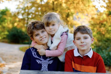 Üç kardeş çocuğunun portresi. İki erkek kardeş erkek kardeş ve küçük tatlı kız kardeş sonbahar parkında birlikte eğleniyorlar. Mutlu sağlıklı aile oyunları, yürüyüş, doğa üzerinde aktif eğlence.