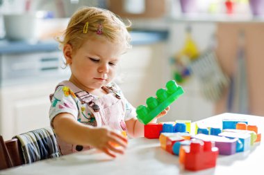 Çocuk odasında ya da evde eğitici oyuncakları olan sevimli bir kız. Mutlu sağlıklı çocuk farklı renkli plastik bloklarla eğleniyor. Sevimli bebek öğrenimi yaratma.