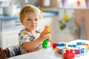 Çocuk odasında ya da evde eğitici oyuncakları olan sevimli bir kız. Mutlu sağlıklı çocuk farklı renkli plastik bloklarla eğleniyor. Sevimli bebek öğrenimi yaratma.