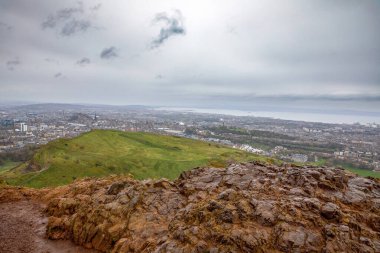 İskoçya, Edinburgh 'daki Arthurs Koltuğundan panoramik manzara, şehir manzarasını sergiliyor, yeşil tepeler yuvarlanıyor, ve bulutlu gökyüzü