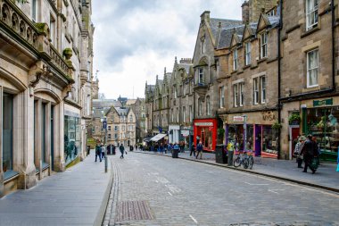 Edinburgh, İskoçya - 13 Nisan 2024: İskoçya 'nın Edinburgh şehrinde tarihi taş binalar, butik dükkanları ve yayaların bulunduğu kaldırım taşı caddesi