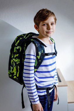 Okul çantalı güzel çocuk sabahın erken saatlerinde odada duruyor. Okula ve derslere giden mutlu sağlıklı çocuk. Eğitim kavramı.