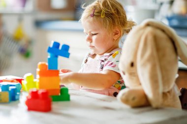 Bebek odasında eğitici oyuncaklarla oynayan pelüş tavşanlı sevimli bir kız. Mutlu sağlıklı çocuk evde renkli farklı plastik bloklarla eğleniyor. Sevimli bebek öğrenimi yaratma