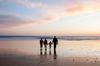 Gün batımında üç çocuk ve babanın resimli mutlu çocukları ve babaları sahilde. Mutlu bir aile, iki okul çocuğu ve küçük bir anaokulu kızı. Kardeşler birlikte eğleniyor. Bağlanma.