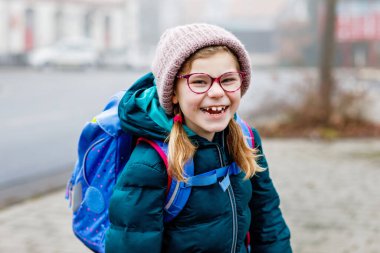 Okula giderken çok tatlı bir kızdı. İlkokula giderken gözlüklü sağlıklı ve mutlu bir çocuk. Okul çantalı gülümseyen çocuk şehir sokaklarında, açık havada. Okula geri dön.