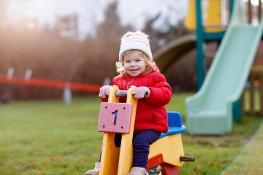 Küçük tatlı kız oyun alanında eğleniyor. Mutlu küçük çocuk tırmanışı, farklı ekipmanların üzerinde sallanmak ve kaymak. Renkli giysiler içinde soğuk bir günde. Çocuklar için aktif açık hava oyunu.