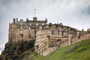 İskoçya 'daki Castle Rock' ın tepesinde tarihi bir kale olan Edinburgh Kalesi 'nin yakın çekimleri, bulutlu bir gökyüzü altında taş duvarlarını ve ikonik mimarisini sergiliyor..