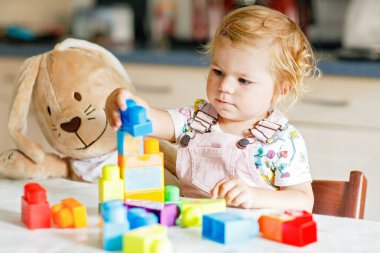 Bebek odasında eğitici oyuncaklarla oynayan pelüş tavşanlı sevimli bir kız. Mutlu sağlıklı çocuk evde renkli farklı plastik bloklarla eğleniyor. Sevimli bebek öğrenimi yaratma