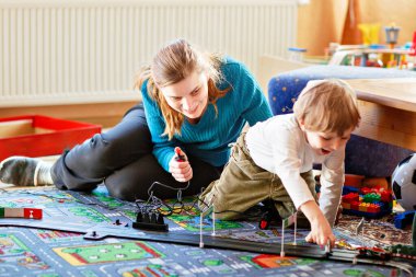 Anne ve oğlu yarış arabalarıyla yarış pistinde, kapalı alanda, arabalarla oynuyorlar. Küçük mutlu anaokulu çocuğu ve genç kadın kapalı alandaki yarış oyunlarıyla eğleniyorlar.