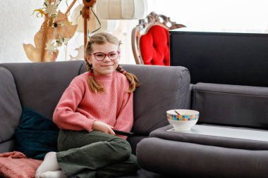 Kahvaltının tadını çıkartan gülümseyen genç bir kız. Yumuşak ışıklandırma ve rahat titreşimlerle sıcak ev atmosferi. Küçük çocuk ve sağlıklı yiyecekler