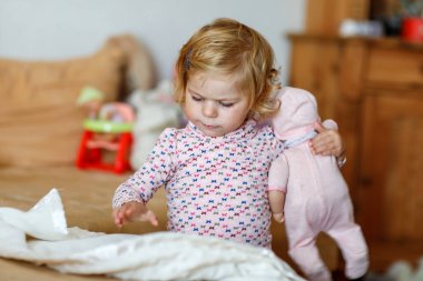 Oyuncak bebekle oynayan sevimli küçük bir kız. Mutlu sağlıklı bebek, rol yapma oyunuyla eğleniyor, evde ya da çocuk odasında annecilik oynuyor. Oyuncaklı aktif kız.
