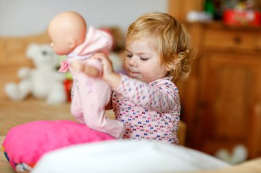 Oyuncak bebekle oynayan sevimli küçük bir kız. Mutlu sağlıklı bebek, rol yapma oyunuyla eğleniyor, evde ya da çocuk odasında annecilik oynuyor. Oyuncaklı aktif kız.