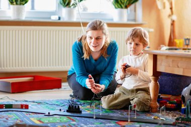 Anne ve oğlu yarış arabalarıyla yarış pistinde, kapalı alanda, arabalarla oynuyorlar. Küçük mutlu anaokulu çocuğu ve genç kadın kapalı alandaki yarış oyunlarıyla eğleniyorlar.