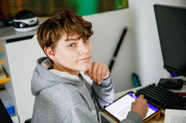 Ergen çocuk evde öğreniyor. Kitap ve tabletle ödev yapan genç bir çocuk. Eğitim, okul kavramı