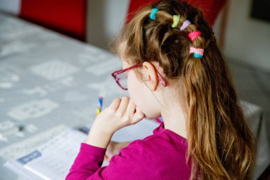 Küçük liseli kız evde öğreniyor. İlkokul öğrencisi Chid matematik ödevi yapıyor, kalemle yazıyor. Gözlüklü mutlu öğrenci..
