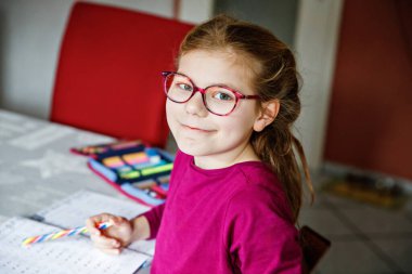 Küçük liseli kız evde öğreniyor. İlkokul öğrencisi Chid matematik ödevi yapıyor, kalemle yazıyor. Gözlüklü mutlu öğrenci..