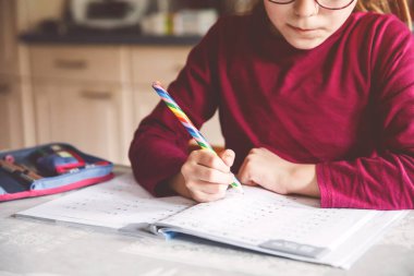 Küçük liseli kız evde öğreniyor. İlkokul öğrencisi Chid matematik ödevi yapıyor, kalemle yazıyor. Gözlüklü mutlu öğrenci..