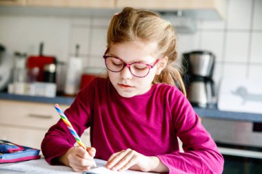 Küçük liseli kız evde öğreniyor. İlkokul öğrencisi Chid matematik ödevi yapıyor, kalemle yazıyor. Gözlüklü mutlu öğrenci..