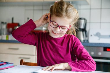 Küçük liseli kız evde öğreniyor. İlkokul öğrencisi Chid matematik ödevi yapıyor, kalemle yazıyor. Gözlüklü mutlu öğrenci..