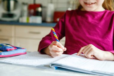Küçük liseli kız evde öğreniyor. İlkokul öğrencisi Chid matematik ödevi yapıyor, kalemle yazıyor. Gözlüklü mutlu öğrenci..
