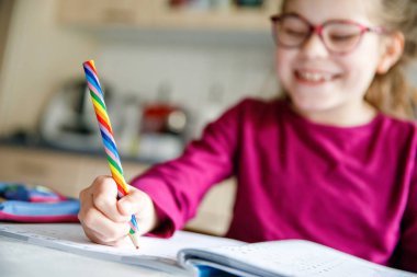 Küçük liseli kız evde öğreniyor. İlkokul öğrencisi Chid matematik ödevi yapıyor, kalemle yazıyor. Gözlüklü mutlu öğrenci..
