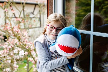 Küçük tatlı kız en sevdiği doldurulmuş hayvan köpekbalığına sarılıyor. Mutlu çocuk