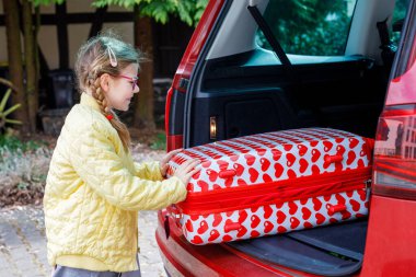 Küçük tatlı kız bavulunu arabaya koydu. Çocuk seyahate çıkar, aile seyahatine çıkar.