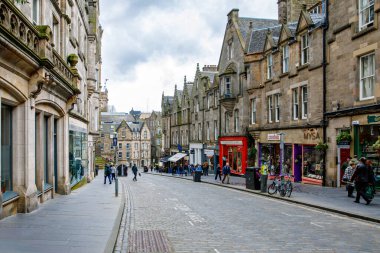 Edinburgh, Scottland - 13 Nisan 2024: İskoçya 'nın Edinburgh şehrinde tarihi taş binalar, butik dükkanları ve yayaların bulunduğu kaldırım taşı caddesi.