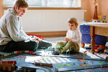 Baba ve oğul yarış arabalarıyla yarış pistinde, kapalı alanda, arabalarla oynuyorlar. Küçük mutlu anaokulu çocuğu ve genç adam kapalı alandaki yarış oyunlarıyla eğleniyor.