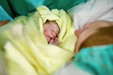 Yeni doğmuş bebek doğumdan sonra battaniyeye sarılmış. Anne ilk kez yeni doğmuş bir kızı arıyor. Yeni doğan çocuk doğumdan saniyeler ve dakikalar sonra. Mutlu anne ağlıyor..