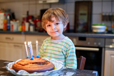 Sevimli dört yaşında bir çocuk doğum gününü kutluyor ve pastadaki mumları içeride üflüyor. Büyük pastalı mutlu çocuk.