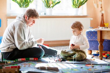 Baba ve oğul yarış arabalarıyla yarış pistinde, kapalı alanda, arabalarla oynuyorlar. Küçük mutlu anaokulu çocuğu ve genç adam kapalı alandaki yarış oyunlarıyla eğleniyor.