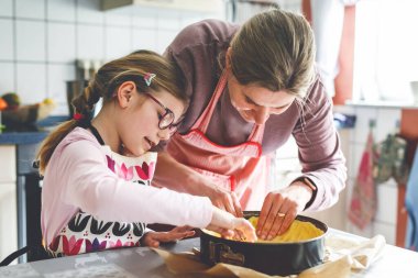 Küçük tatlı kız annesinin mutfakta kek pişirmesine yardım ediyor. Çocuk ve kadın malzemeleri neşeyle harmanlıyor, sıcak, ev ortamında yemek yapmayı öğreniyor..