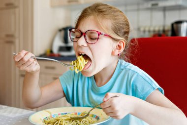 Evde yeşil soslu spagetti yiyen küçük liseli kız. Gözlüklü şirin, mutlu çocuk sağlıklı öğle yemeği yiyor.