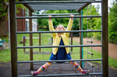 Küçük kız tırmanma iskeletinde jimnastik yapıyor, okul bahçesinde yatay bar. Çocuk okul tatilinde eğleniyor