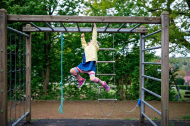 Küçük kız tırmanma iskeletinde jimnastik yapıyor, okul bahçesinde yatay bar. Çocuk okul tatilinde eğleniyor