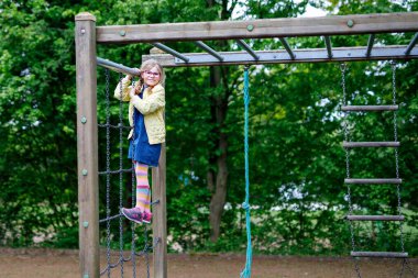 Küçük kız tırmanma iskeletinde jimnastik yapıyor, okul bahçesinde yatay bar. Çocuk okul tatilinde eğleniyor